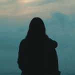 Woman staring into the greenish cast of a sunset while contemplating the weekly horoscope for April 12-18, 2026