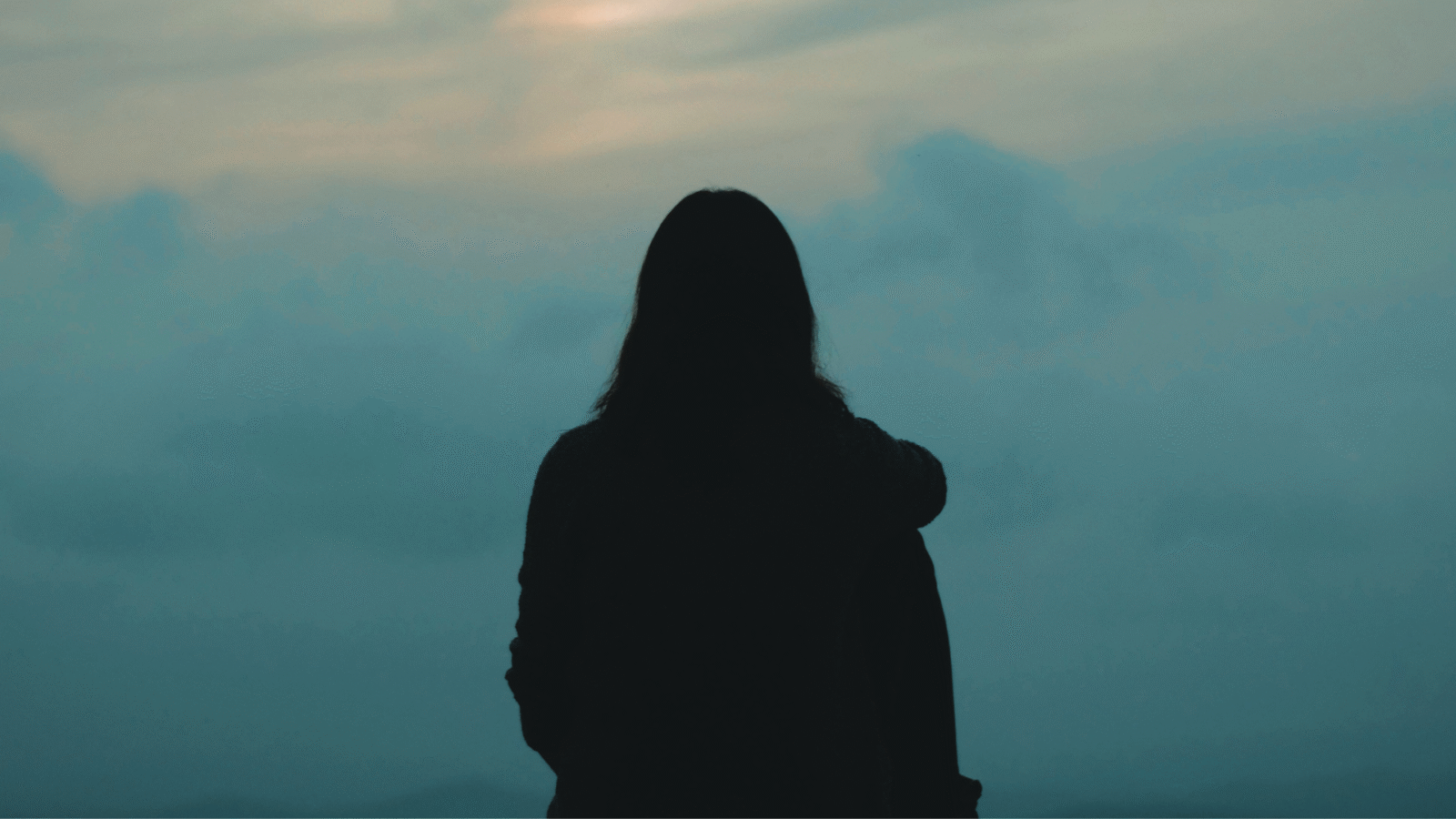 Woman staring into the greenish cast of a sunset while contemplating the weekly horoscope for April 12-18, 2026