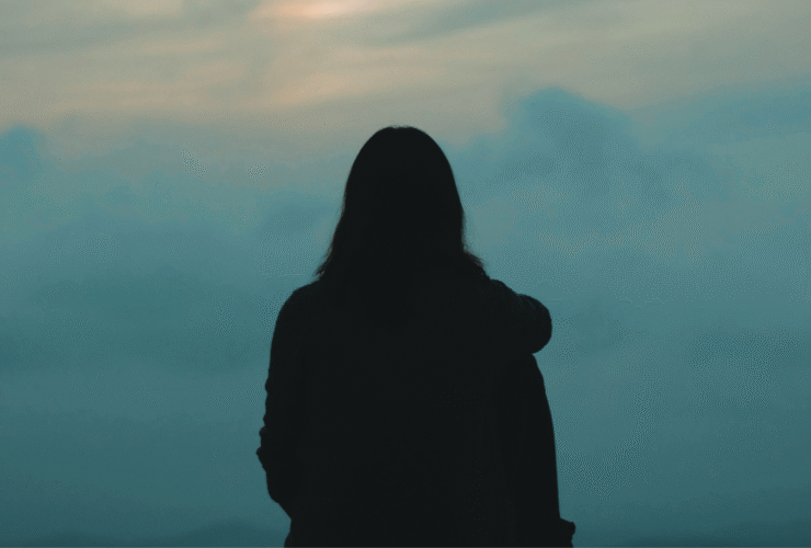 Woman staring into the greenish cast of a sunset while contemplating the weekly horoscope for April 12-18, 2026